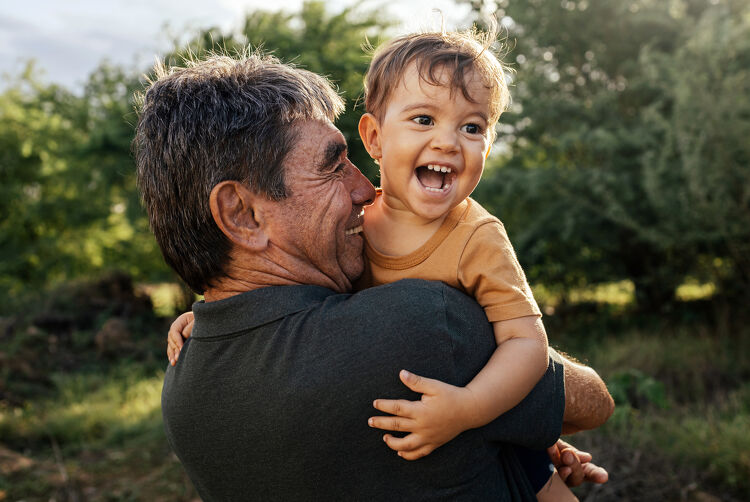 Grandfather joyfully holding his grandchild outside, representing family security with a home loan
